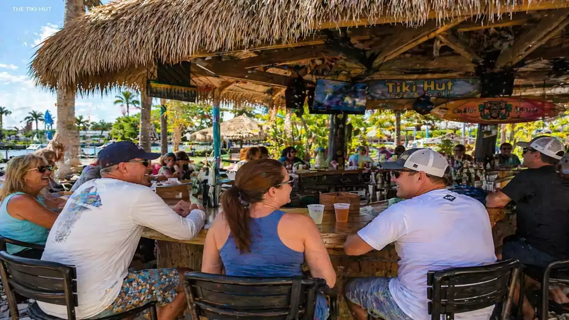 People sitting at a table in a tropical beach bar with a thatched roof.