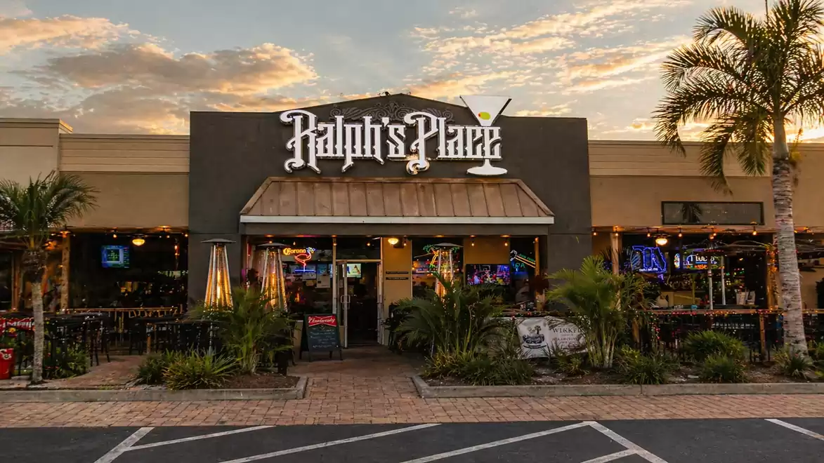 Exterior view of a restaurant at sunset with palm trees and lively atmosphere.