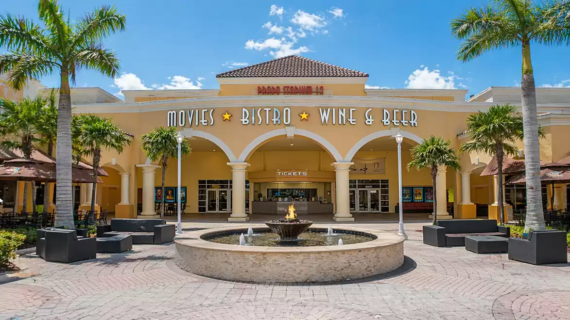 Image shows a cinema with bistro, wine, and beer, surrounded by palm trees and a fountain in the foreground.