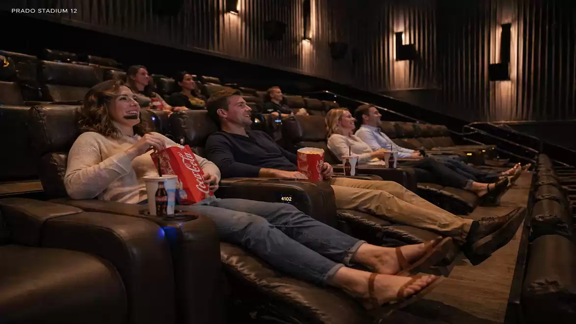 Cinema-goers sitting in comfortable seats enjoying a movie with popcorn and drinks.