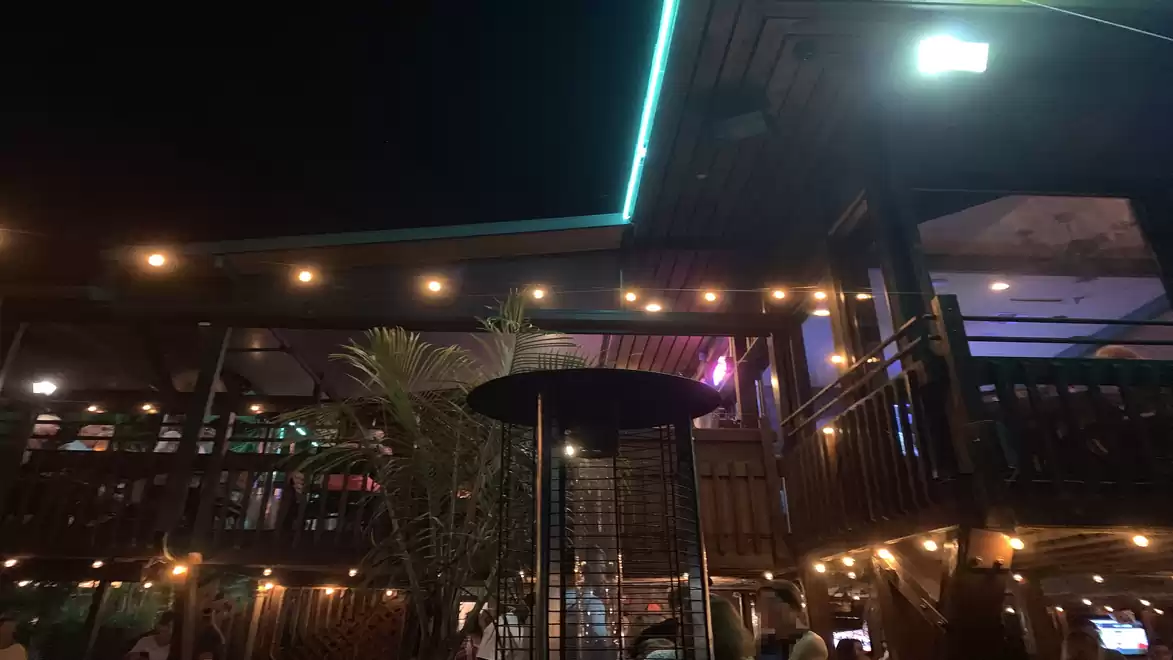 Night view of a cozy outdoor restaurant area with string lights, modern terrace structure, and plants.