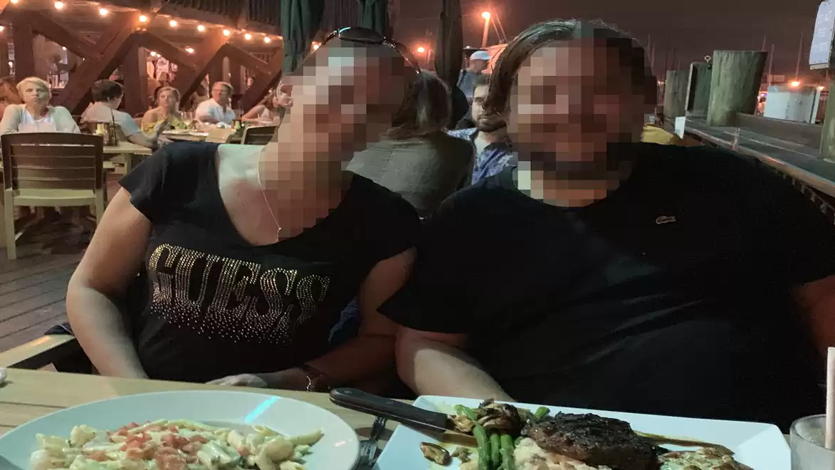 Two people sitting at an outdoor dinner, surrounded by other guests and string lights.