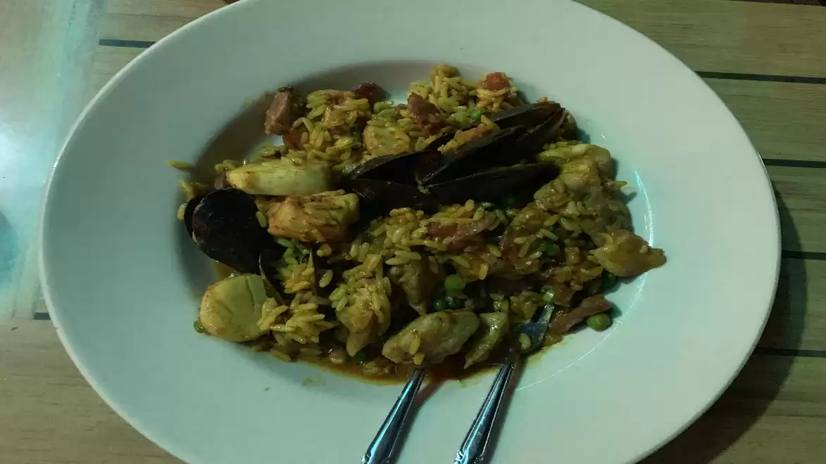 A plate of paella filled with seafood such as mussels and shrimp, served on a wooden table.