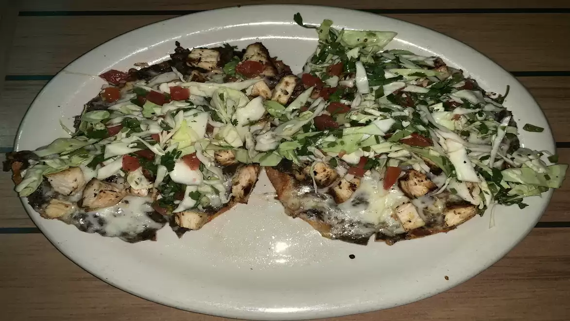 Two topped tortillas on a white plate with grilled chicken, melted cheese, tomatoes, and fresh cabbage.