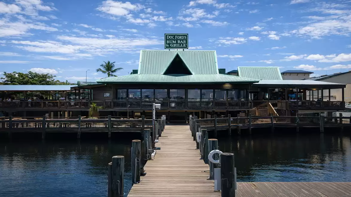 Wooden pier leading to a waterfront restaurant with a green roof and blue sky