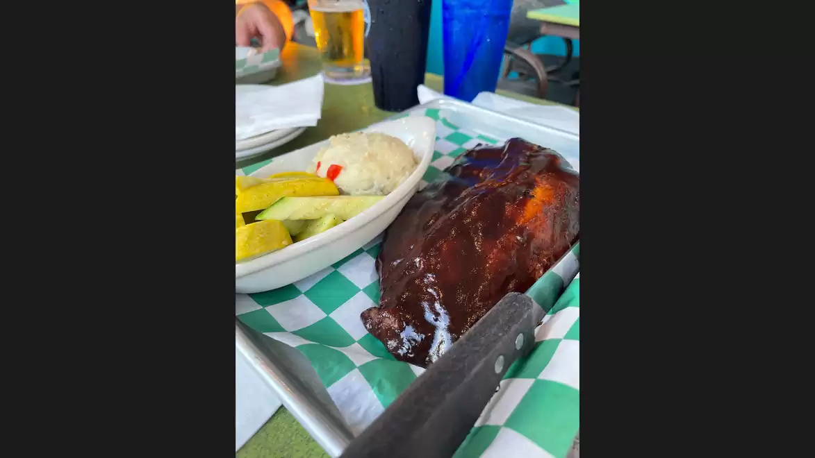 A plate of barbecue ribs with a side of coleslaw and pickles on a table.