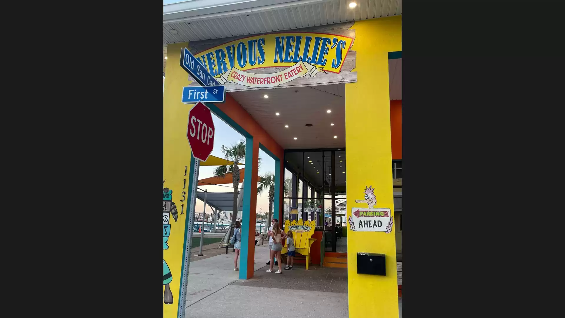 Colorful exterior view of a restaurant with a yellow and blue sign above the entrance, relaxed street scene with stop sign and directional sign.