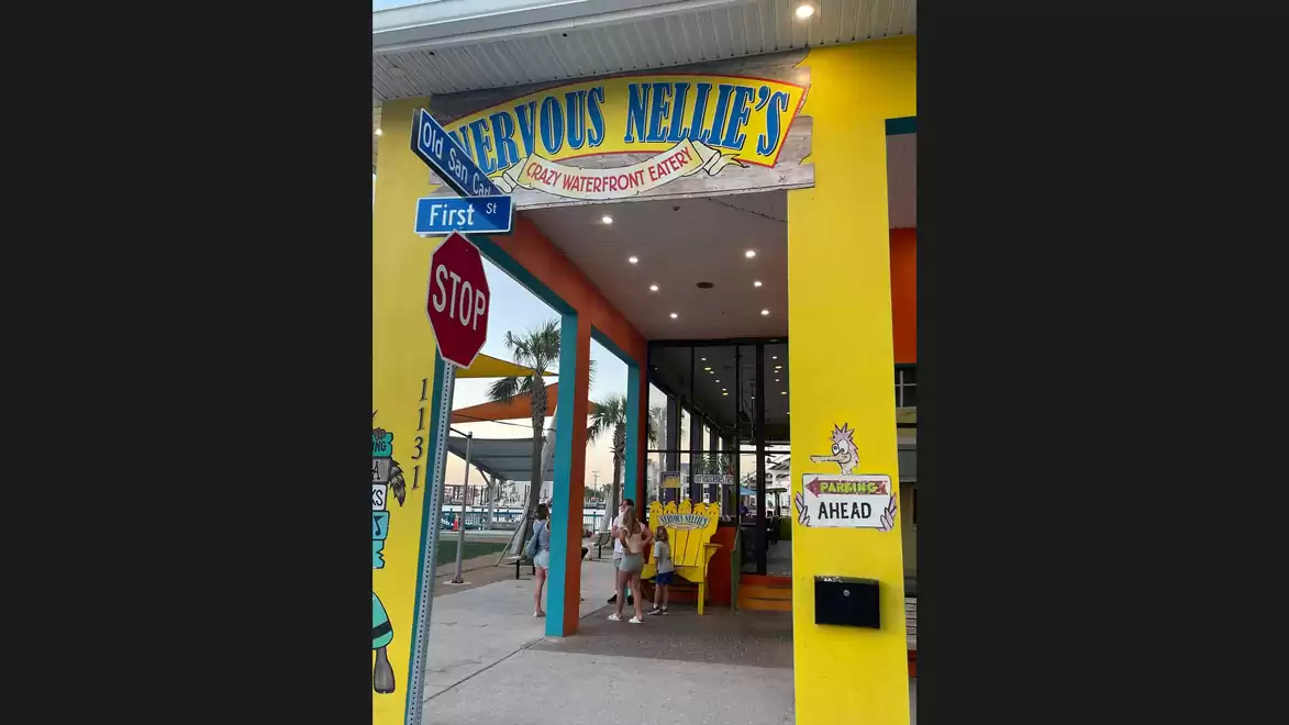 Colorful exterior view of a restaurant with a yellow and blue sign above the entrance, relaxed street scene with stop sign and directional sign.