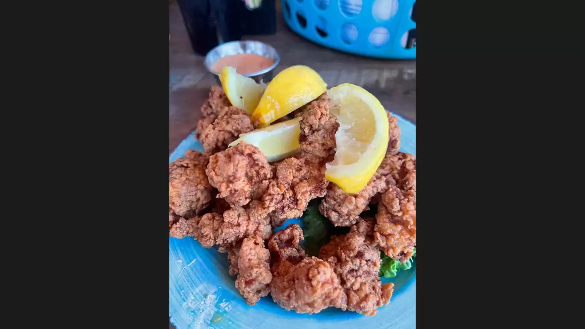 A plate of crispy fried chicken garnished with lemon slices and a side of dipping sauce in the background.