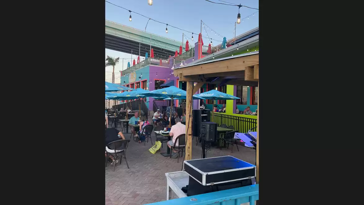 A vibrant outdoor area of a colorful bar or restaurant with blue umbrellas and guests sitting at tables.