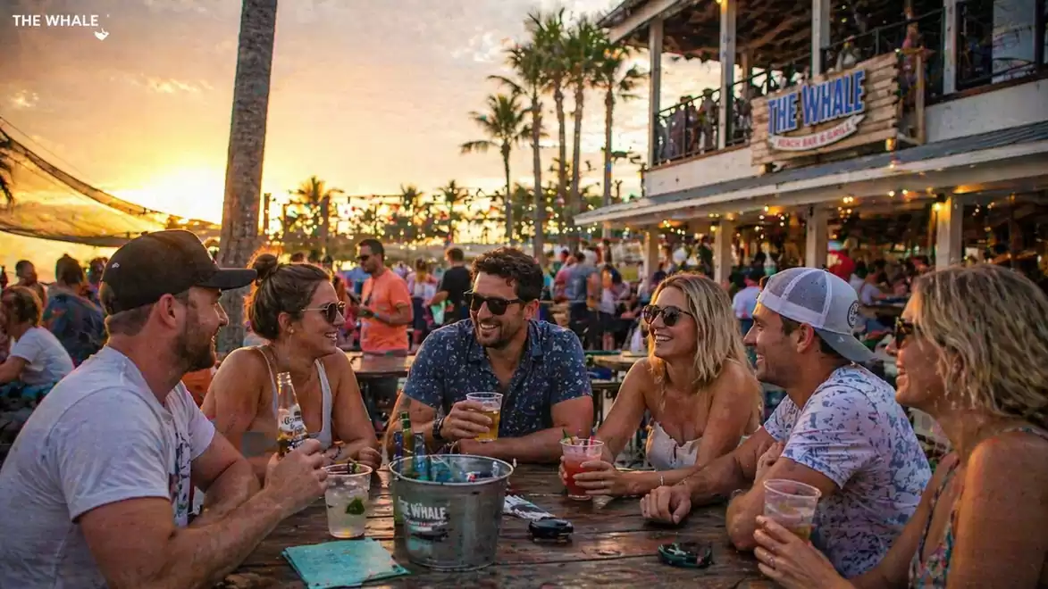 A group of people sitting at a lively beach restaurant enjoying drinks at sunset.