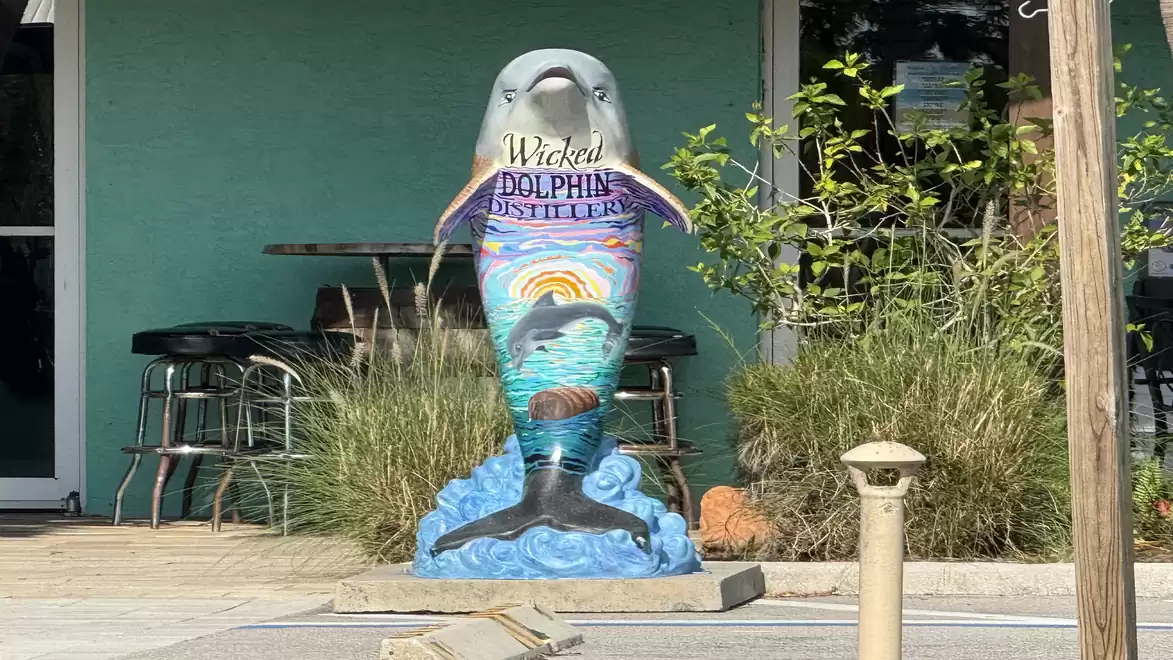 Artistically painted dolphin in front of a green building, surrounded by plants.