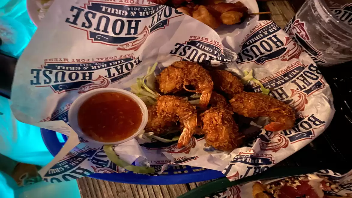 A plate of fried shrimp with a bowl of red sauce, served on printed paper with a restaurant's logo.