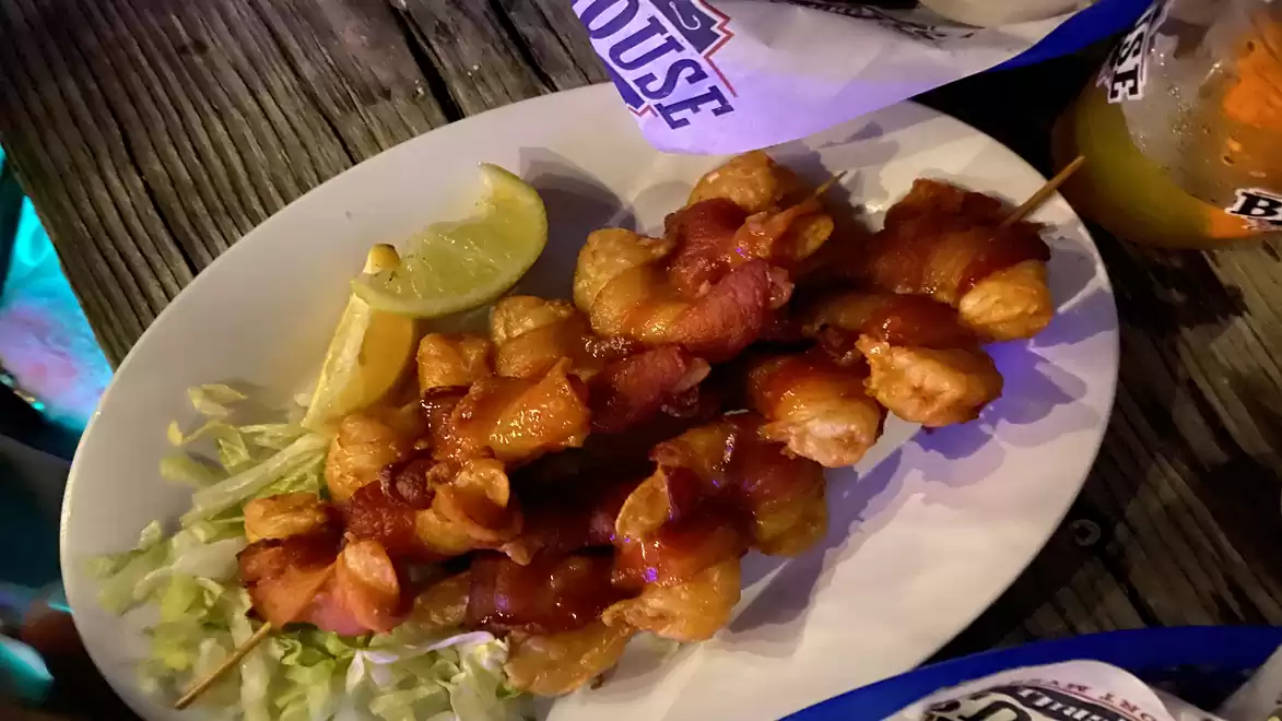 Close-up of two skewers with fried dough on a white plate, accompanied by lime wedges and salad on a wooden table.