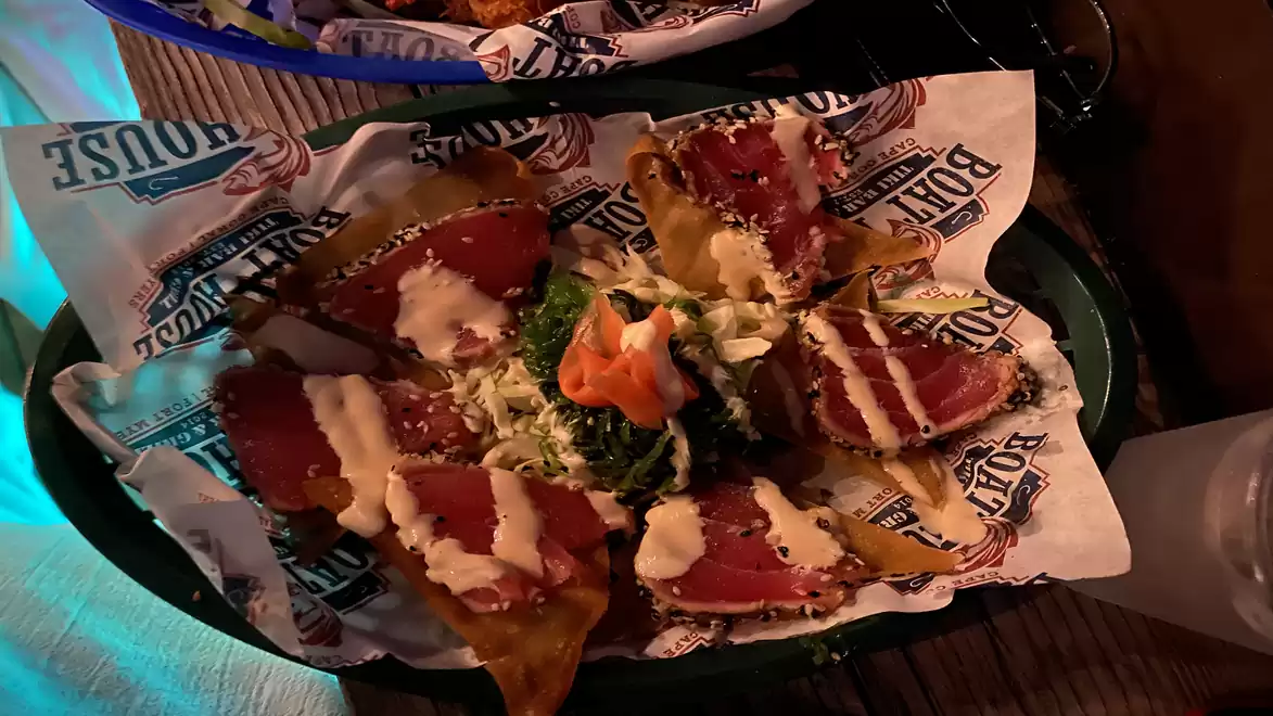 A plate of tuna tacos, garnished with vegetables and a cream sauce, served on printed paper and a green plate.