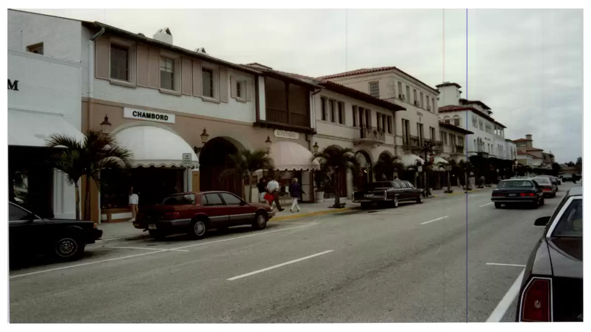 A street scene of a shopping street with historic buildings, cars, and palm trees by the roadside.