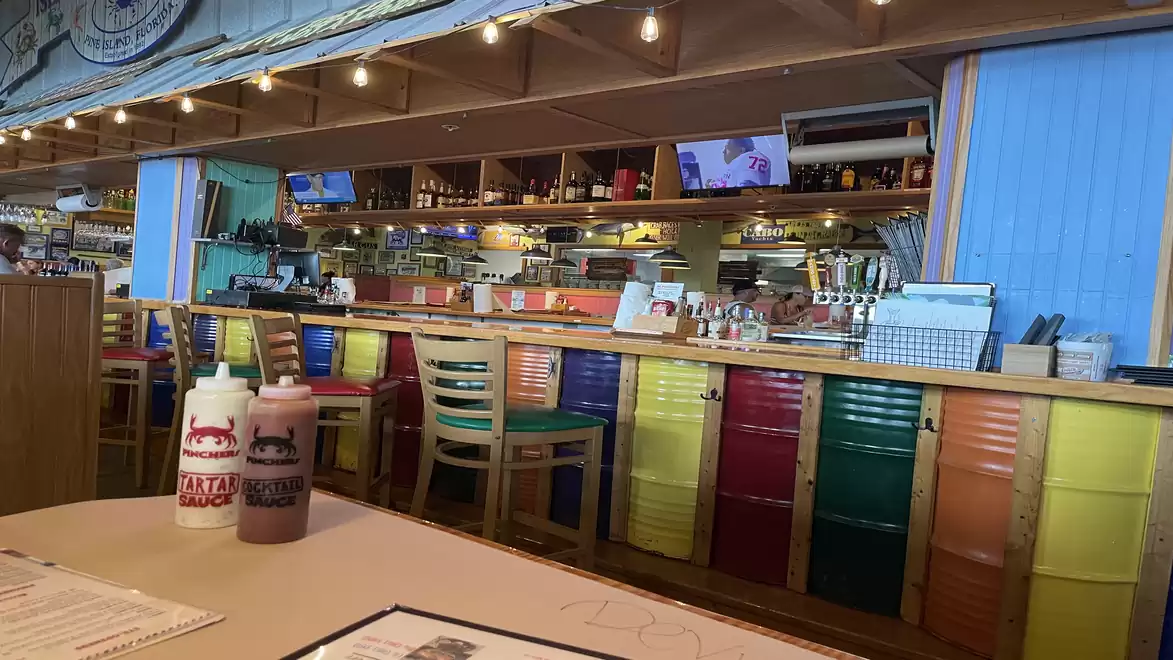 Interior of a colorful cafe with vibrant chairs and a bar with drinks and sauce bottles on the table.