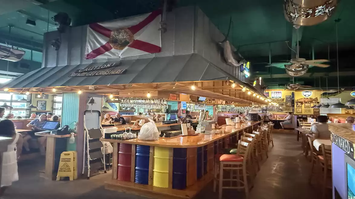 Interior view of a cozy restaurant with a long bar, colorful stools, and a flag hanging from the ceiling.