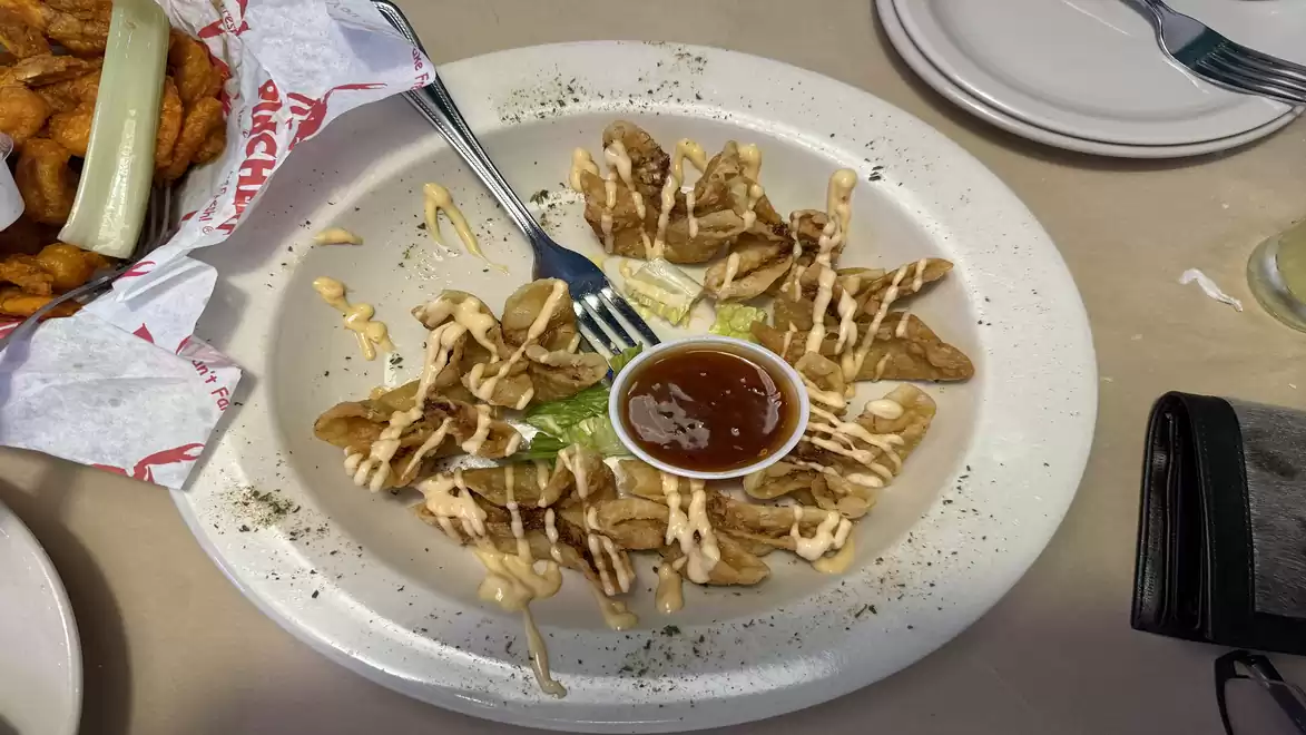 A plate of fried potato wedges, garnished with a creamy sauce, served with a bowl of ketchup in the center.