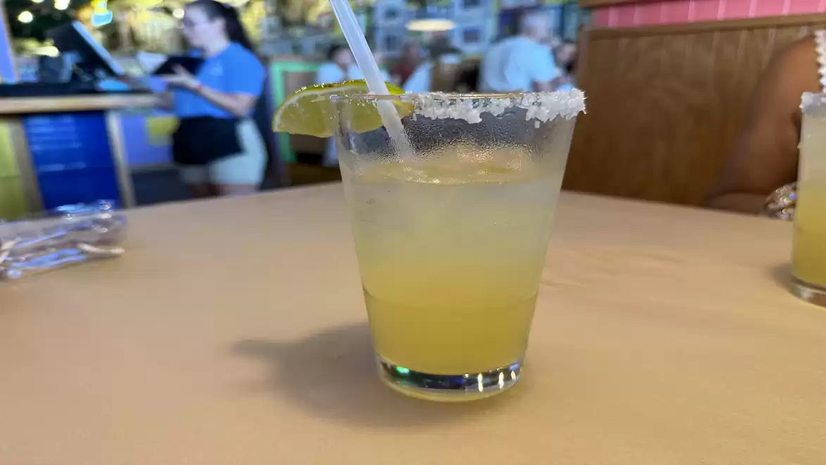 A margarita glass with a salted rim and lime slice sits on a table in a restaurant.