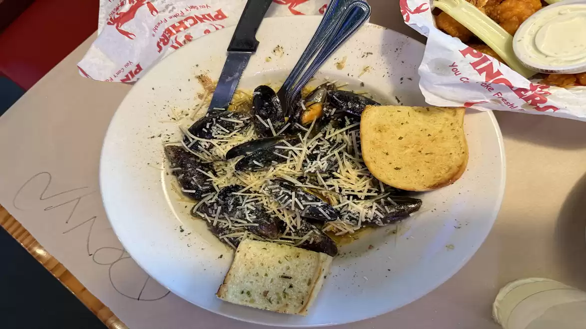 A plate of mussels covered with cheese, accompanied by two slices of bread. Served on a table with napkins in the background.