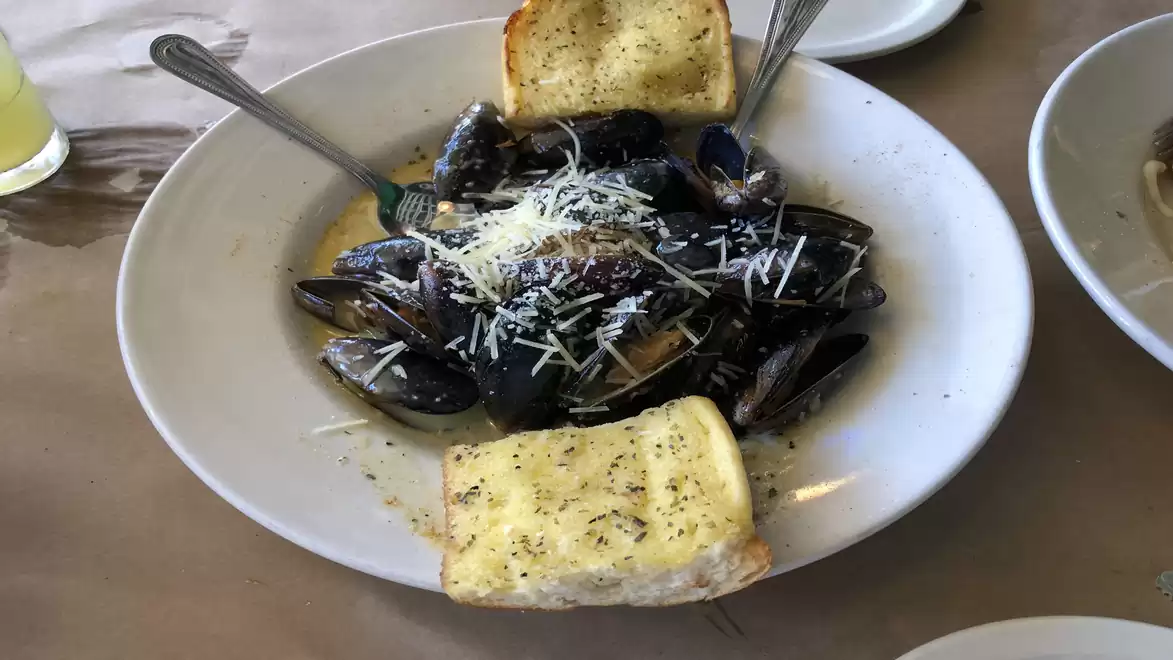 A plate of mussels topped with grated cheese, served with two slices of garlic bread.
