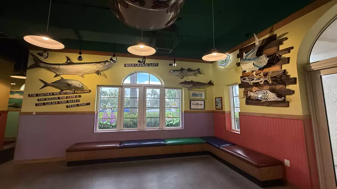A room with benches under a window, displaying mounted fish on the walls. The wall design is colorful with yellow and red tones.
