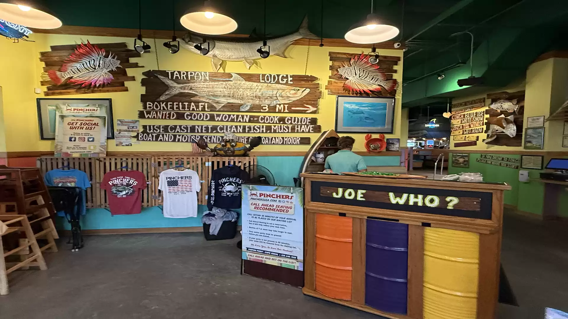 Interior view of a rustic restaurant with colorful counter 'JOE WHO?', decorations, and signs on the walls.