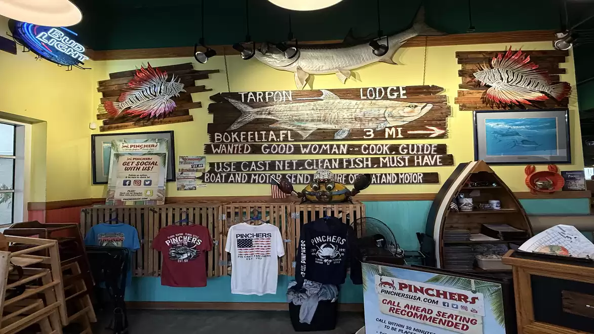Interior of a rustic restaurant featuring decorative fish motifs on the wall and merchandising items like T-shirts on a wooden panel.