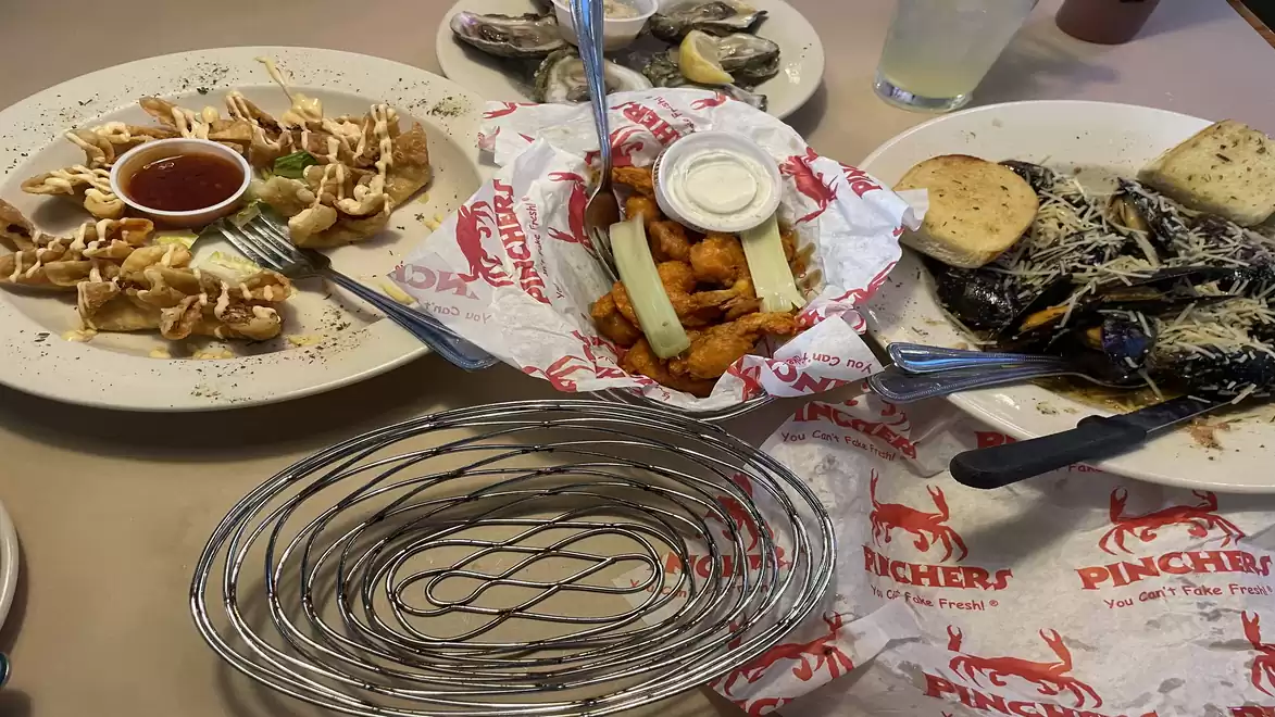A table with various seafood dishes, including shrimp with cocktail sauce, mussels with parmesan and garlic bread, and a basket of fried items.