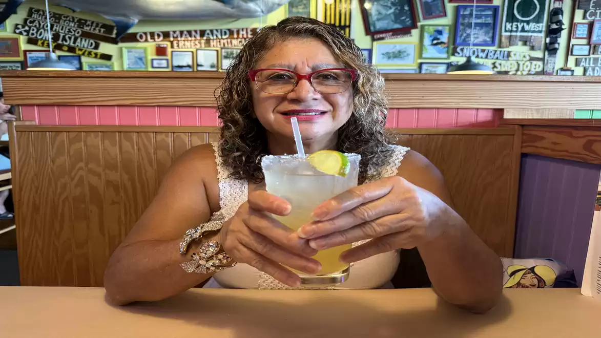 Woman with red glasses sitting in a restaurant holding a drink with lemon and straw.