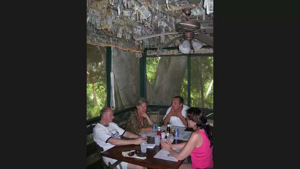 A group of four people sitting at a table in a room with a ceiling covered in dollar bills and large windows overlooking a garden.
