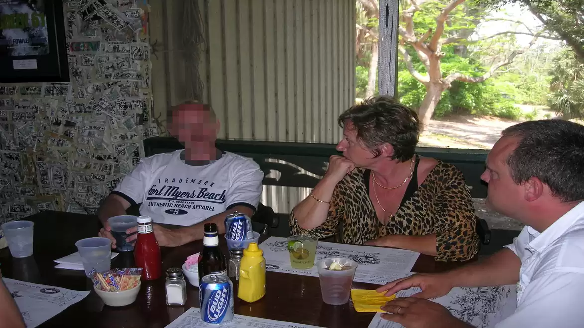 Four people sitting at a table in a restaurant, with drinks, ketchup, and mustard in the middle, engaging in conversation.
