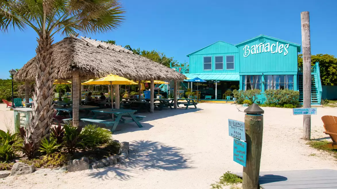 Beach restaurant with a thatched-roof pavilion and colorful umbrellas on a sunny day.