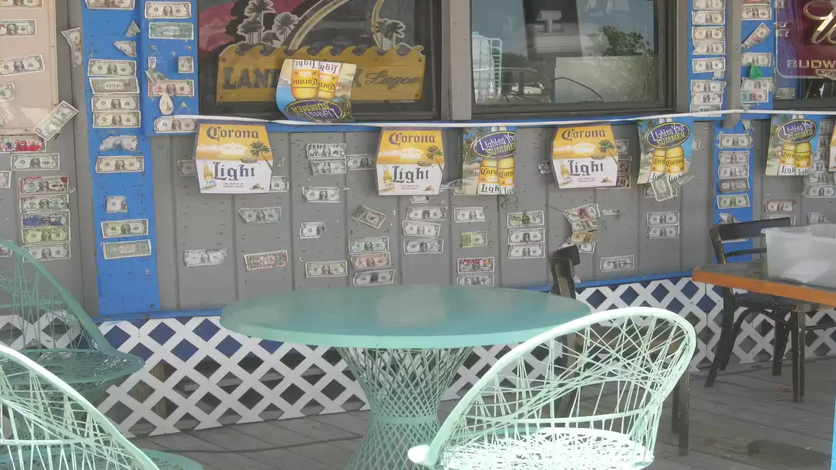 An outdoor table with wire chairs in front of a wall decorated with dollar bills and Corona Light banners.