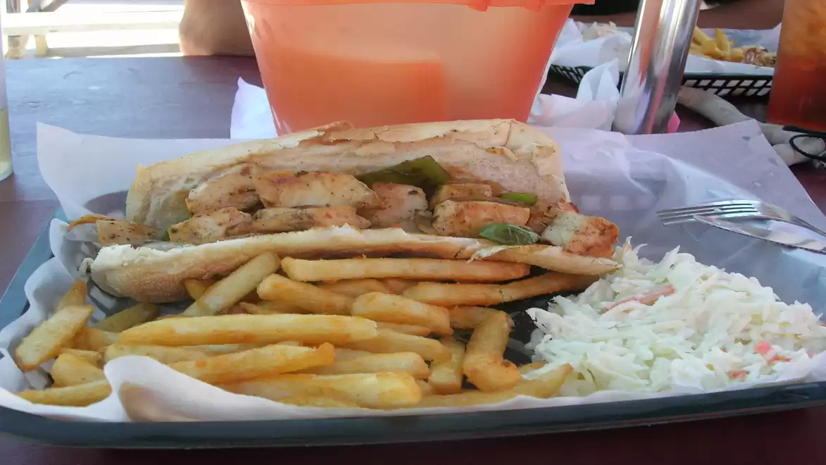 A tray with a sandwich filled with meat and vegetables, served with French fries and coleslaw.