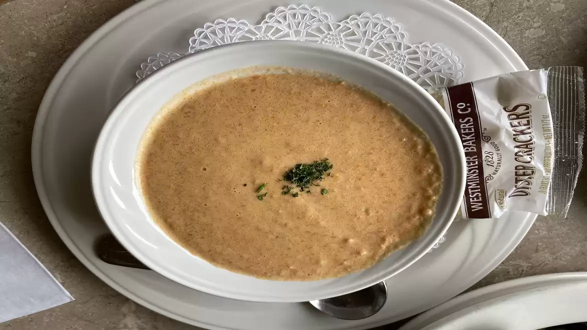 Bowl of creamy soup, garnished with parsley and served on a plate with crackers.