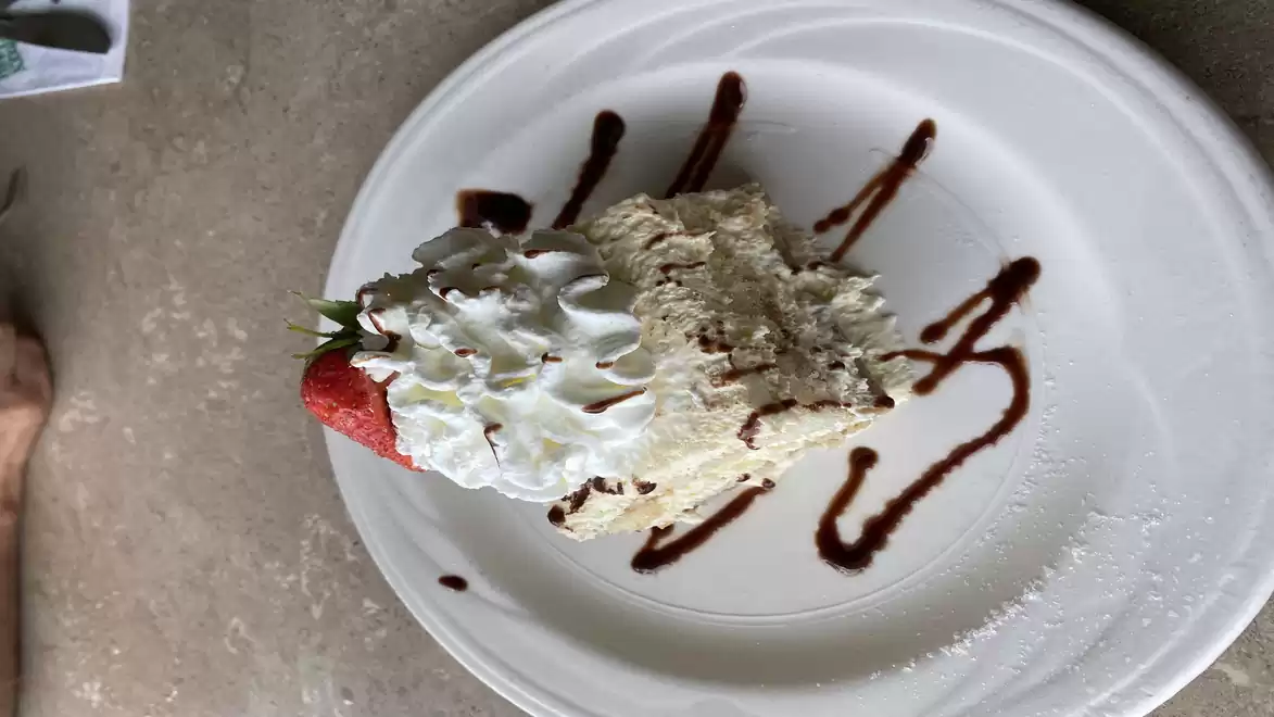 A delicious dessert on a white plate. A piece of cake with cream, strawberry, and chocolate sauce.