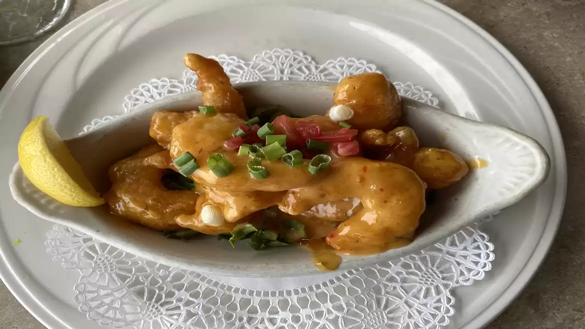 An elegant plate with golden fried shrimp, garnished with spring onions and a lemon wedge.
