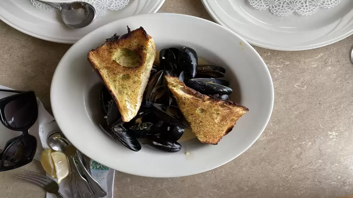 A plate of mussels served with two pieces of toasted bread on a table.