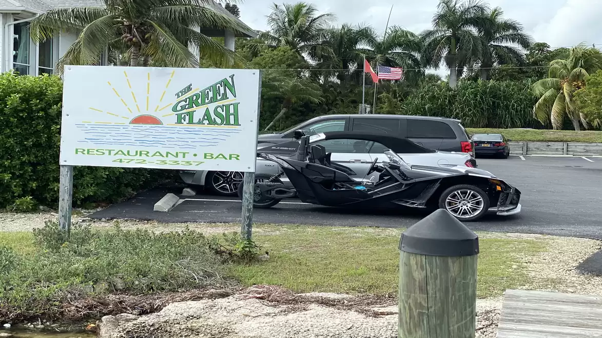 Image of a parking lot in front of the 'Green Flash' restaurant, with a modern car in the foreground and palm trees in the background.