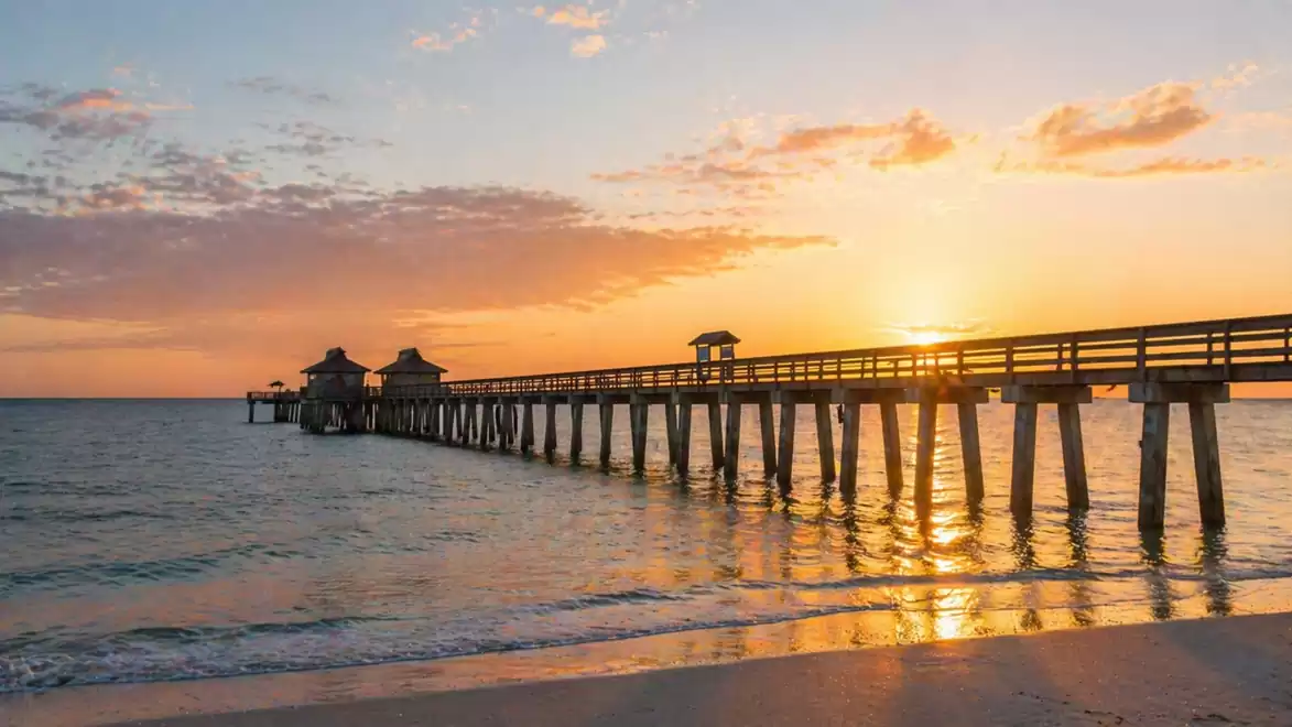 An idyllic sunset at the beach with a long wooden pier extending into the sea.