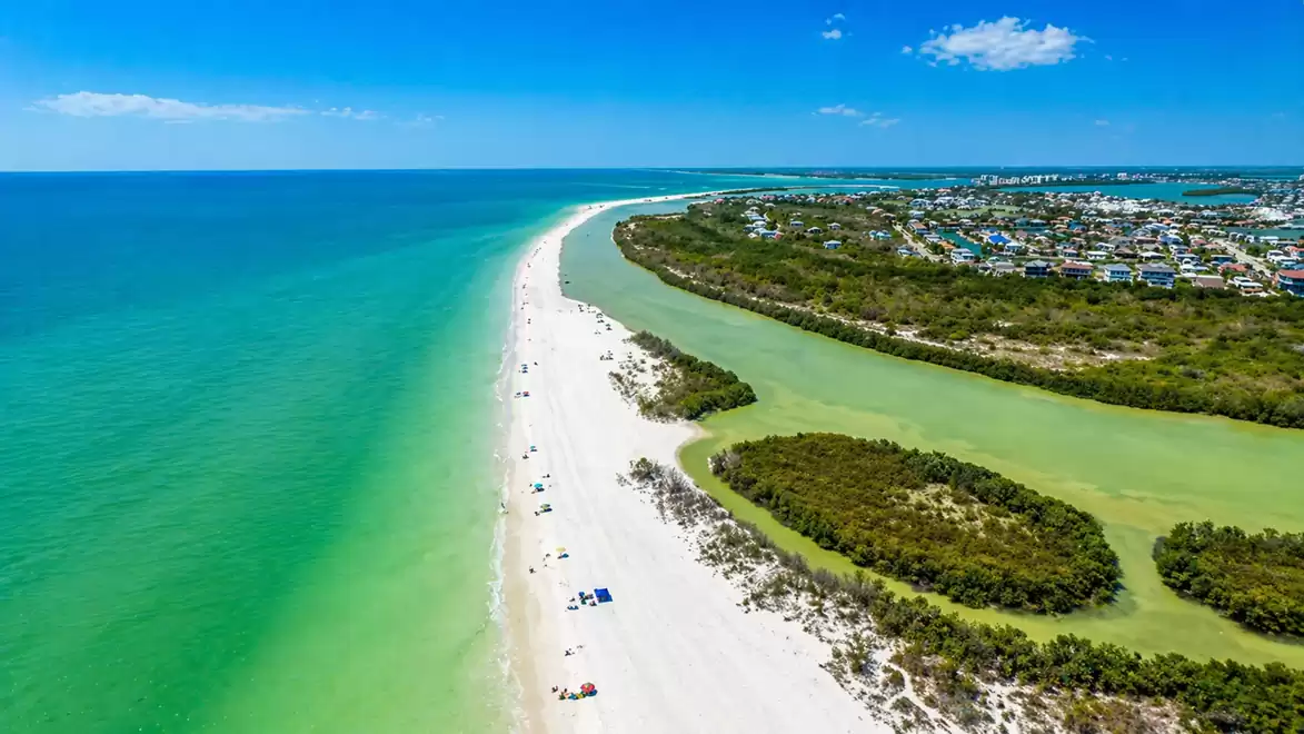 Aerial view of a stunning coastline with white sandy beach, turquoise water, and an adjacent city under a blue sky.