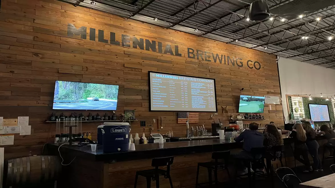 Interior of a brewery with wooden walls, several TVs, and people at the bar.