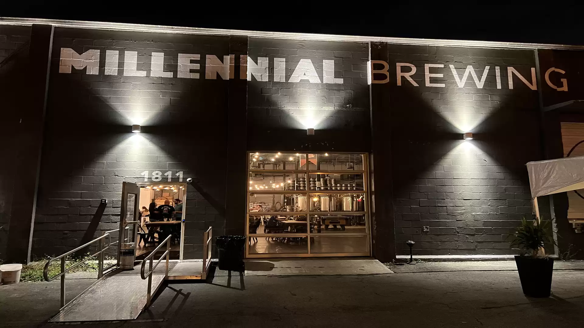 Exterior view of a brewery at night with illuminated sign 'Millennial Brewing' and glass front.