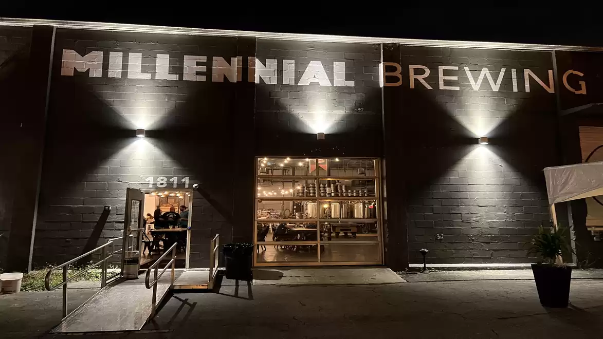 Exterior view of a brewery at night with illuminated sign 'Millennial Brewing' and glass front.