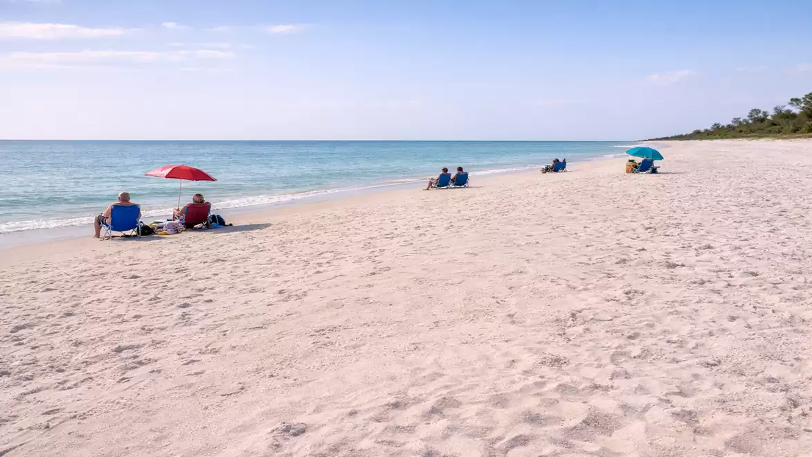 A peaceful beach with fine sand and clear blue water. Some people relax under sun umbrellas along the shore.