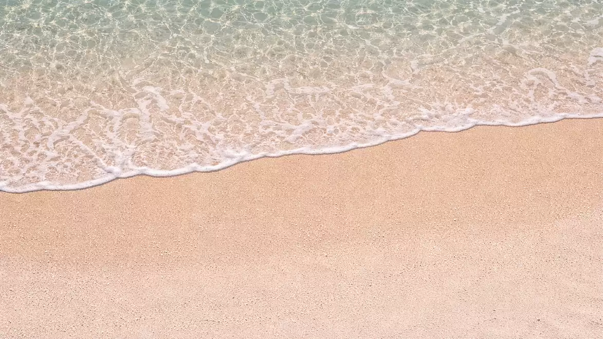 A tranquil sandy beach with gentle waves reaching the clear blue waters of the sea.