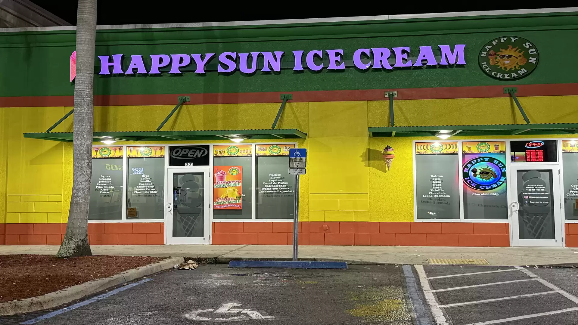 Colorful ice cream shop named Happy Sun Ice Cream, lit up at night.