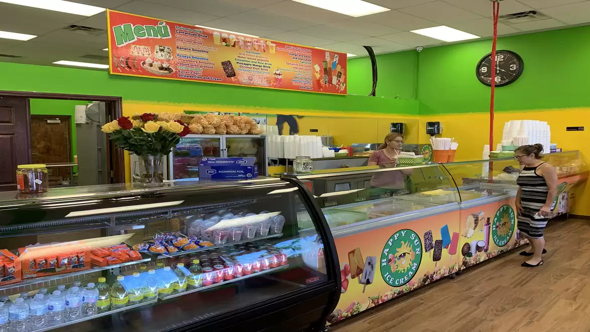 Interior view of a colorful ice cream shop with green and yellow walls, ice cream counter, and decorations, a customer standing in front of the counter.